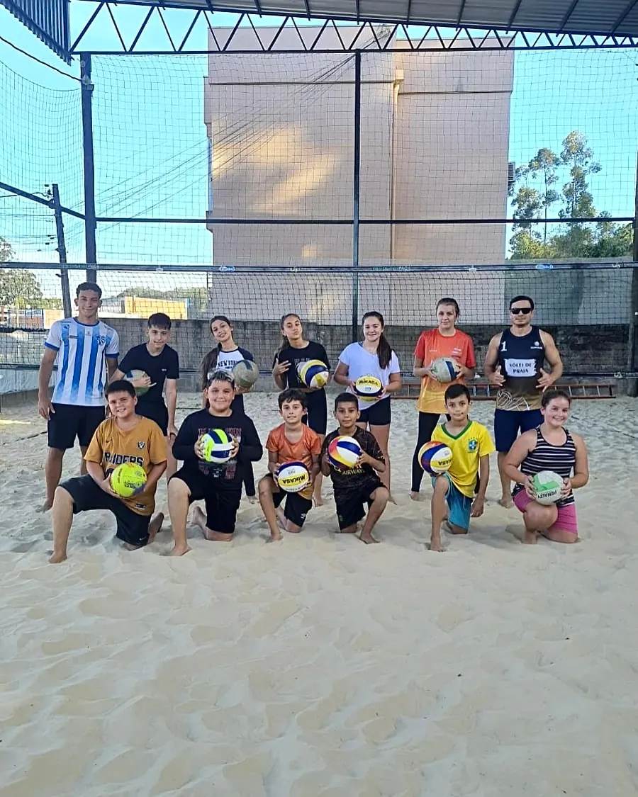 Turma de crianças e adolescentes do vôlei posando com as bolas na areia