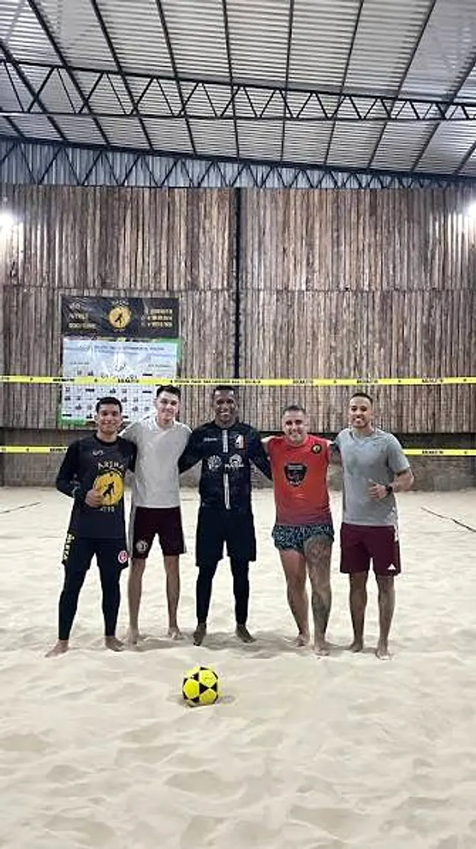 Cinco jogadores de futevôlei abraçados na quadra, em jogo à noite