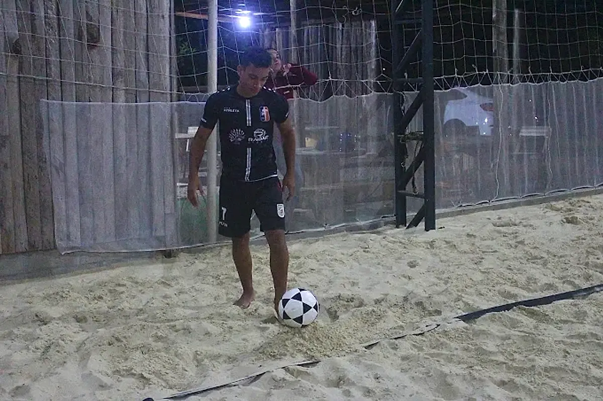Jogador dominando a bola de futevôlei na areia, em jogo à noite