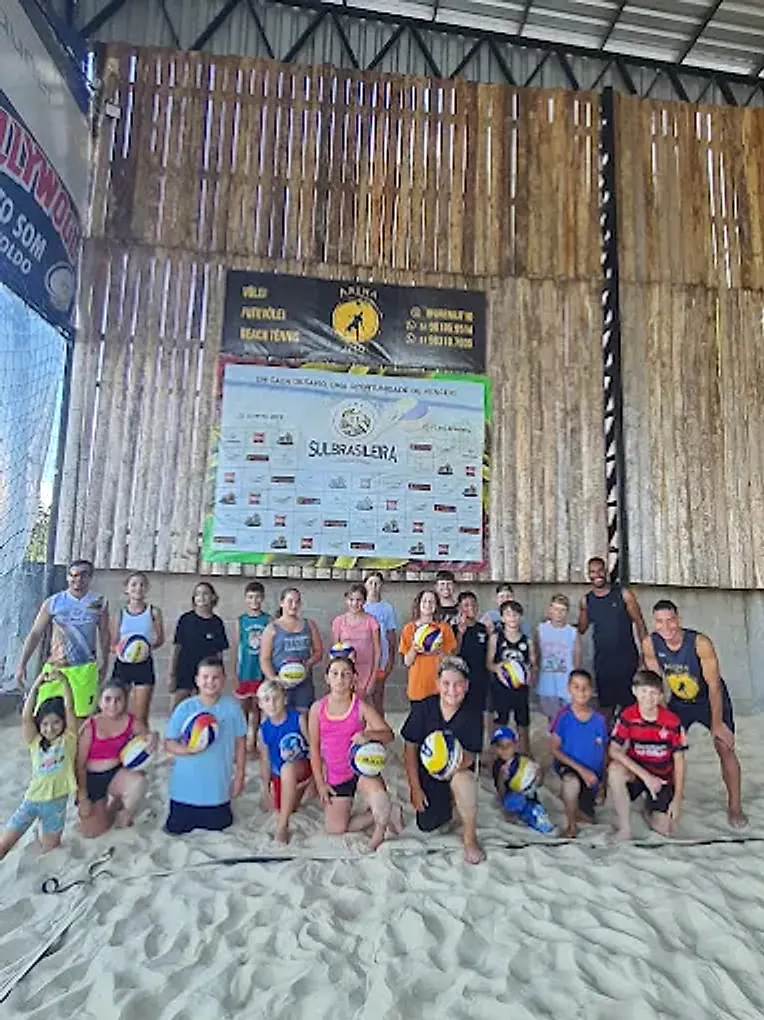 Turma grande de alunos de vôlei posando na areia da Arena JT10